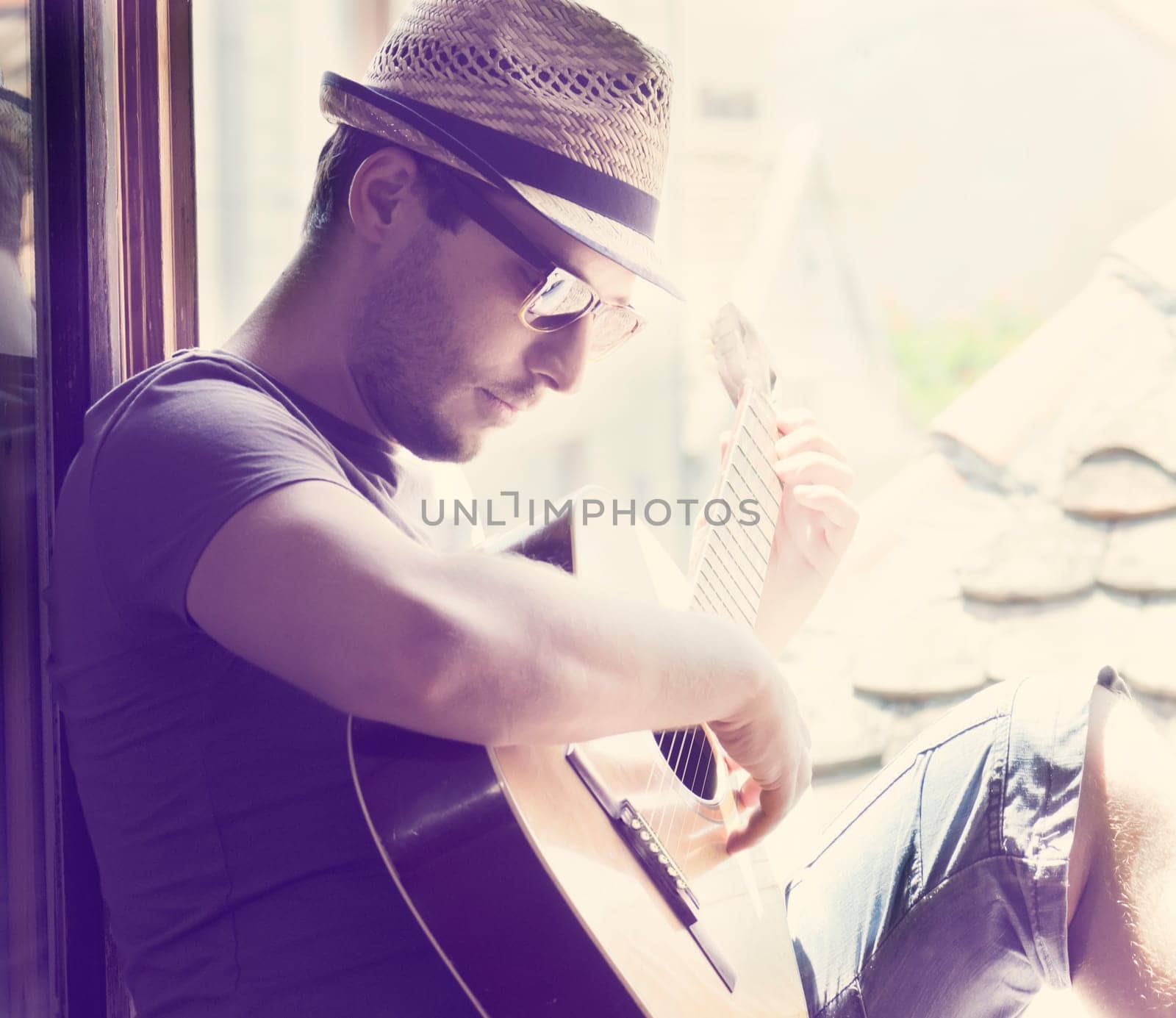 Young man sitting on the window playing the guitar