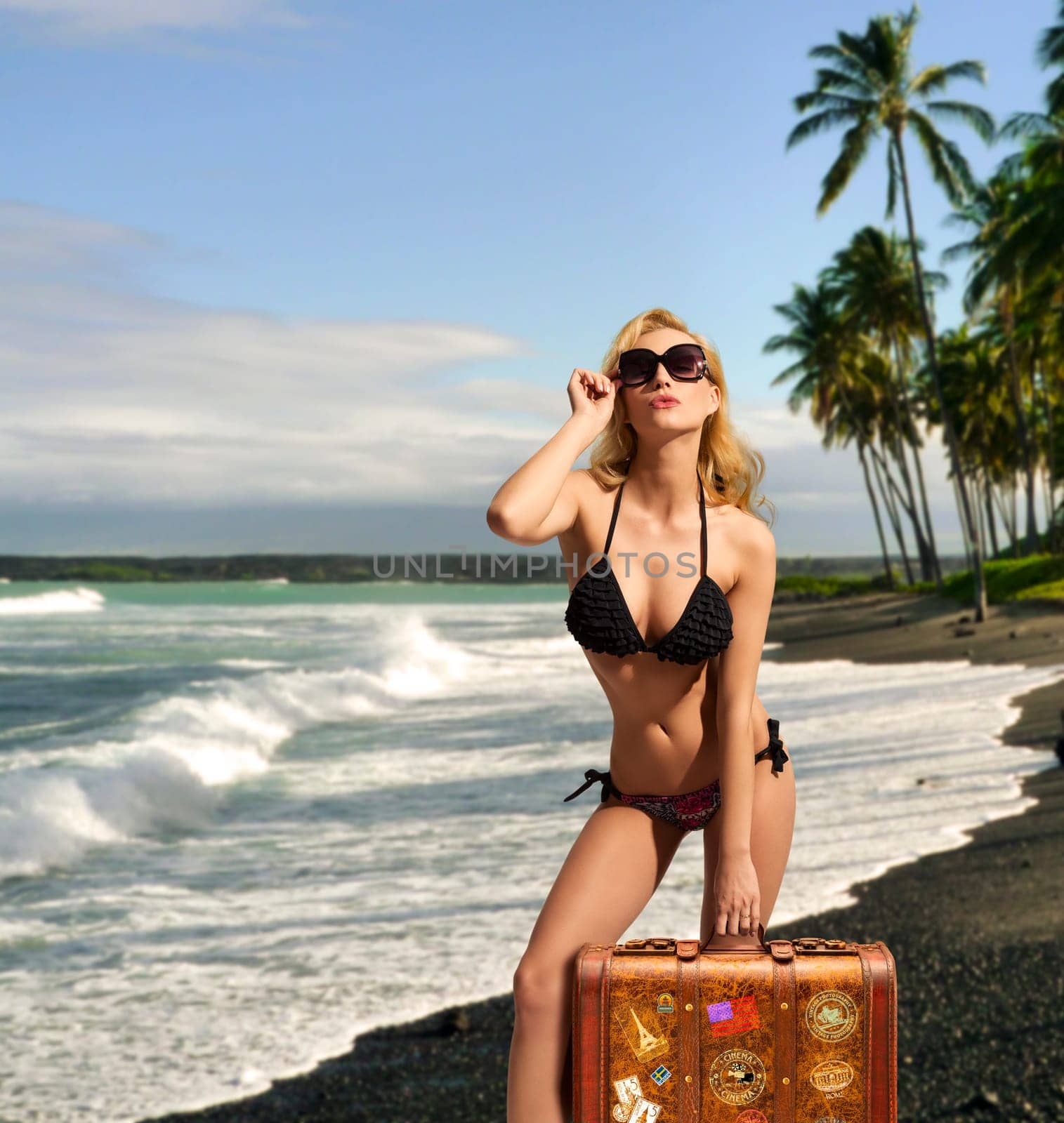 cute blonde woman in provocative pose wearing  sexy bikini, sunglasses and heels and taking one bag on tropical background