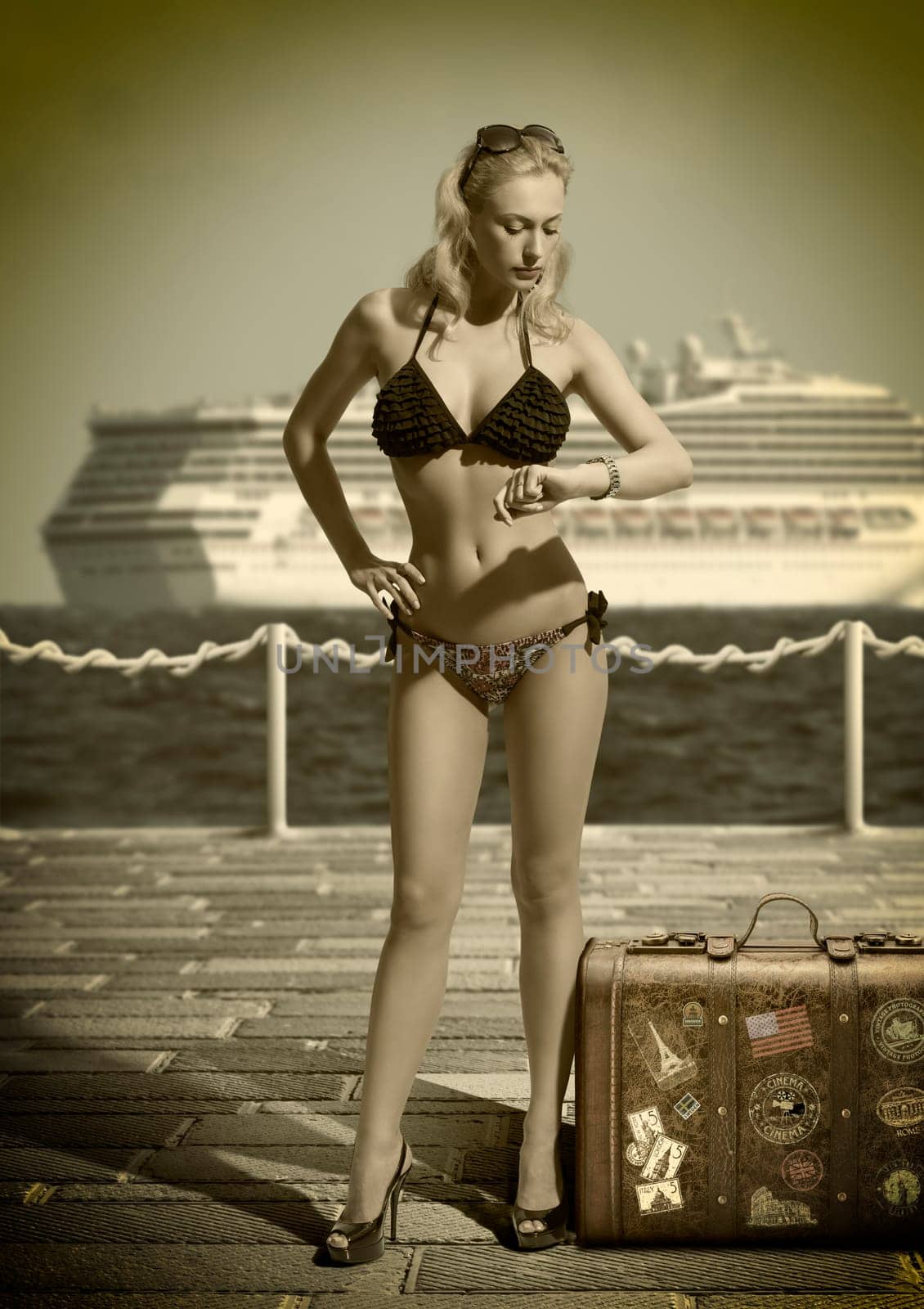 vintage shot of blond girl in bikini in pier eith pld fashion suitcase looking watch with a cruiser ship on background