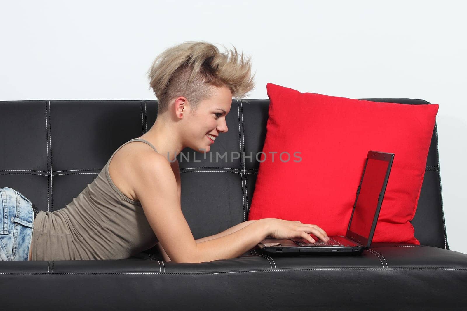 Fashion woman browsing internet in a laptop at home lying on a black couch