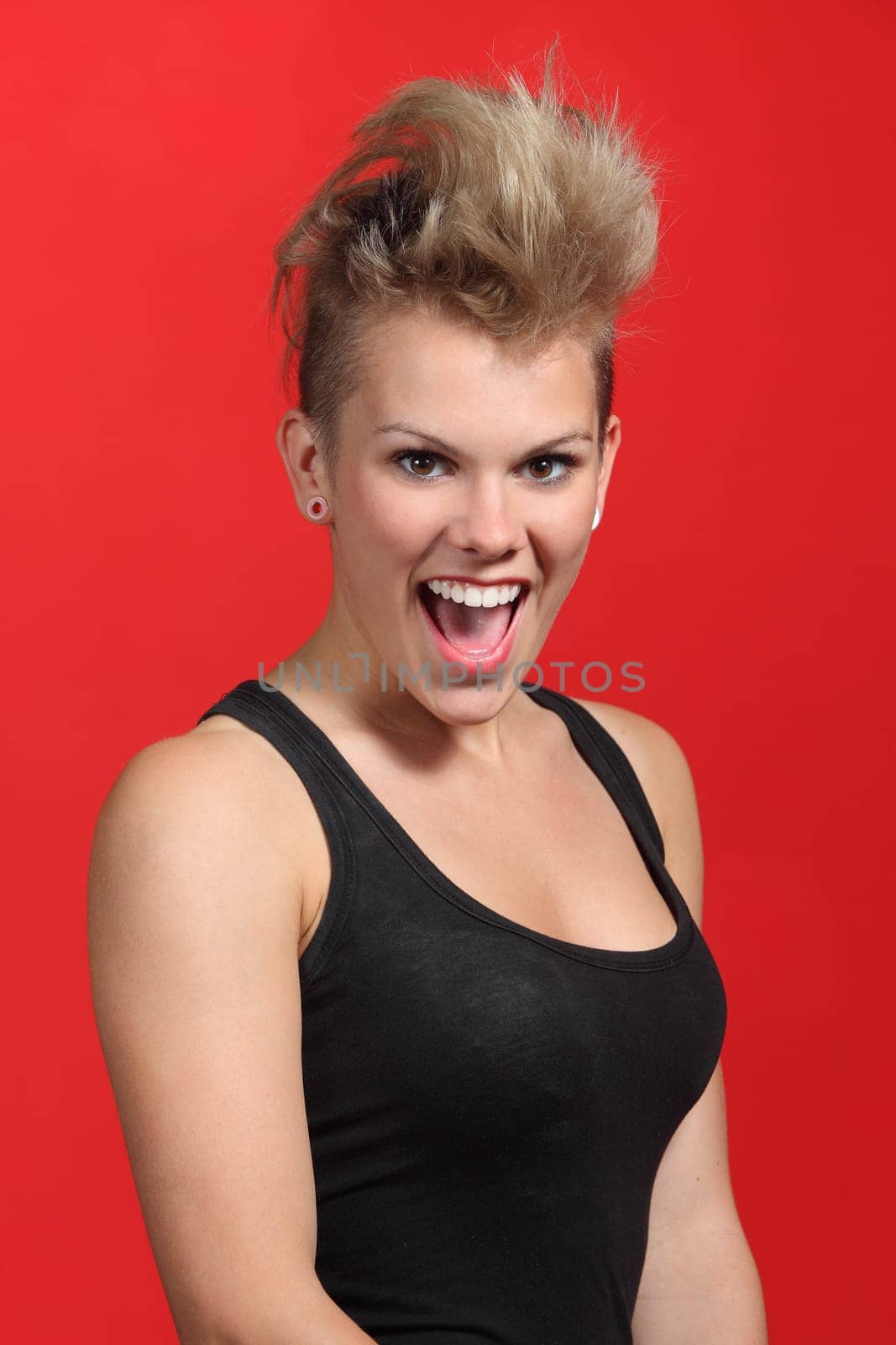 Portrait of a fashion punk hair style woman excited on a red background