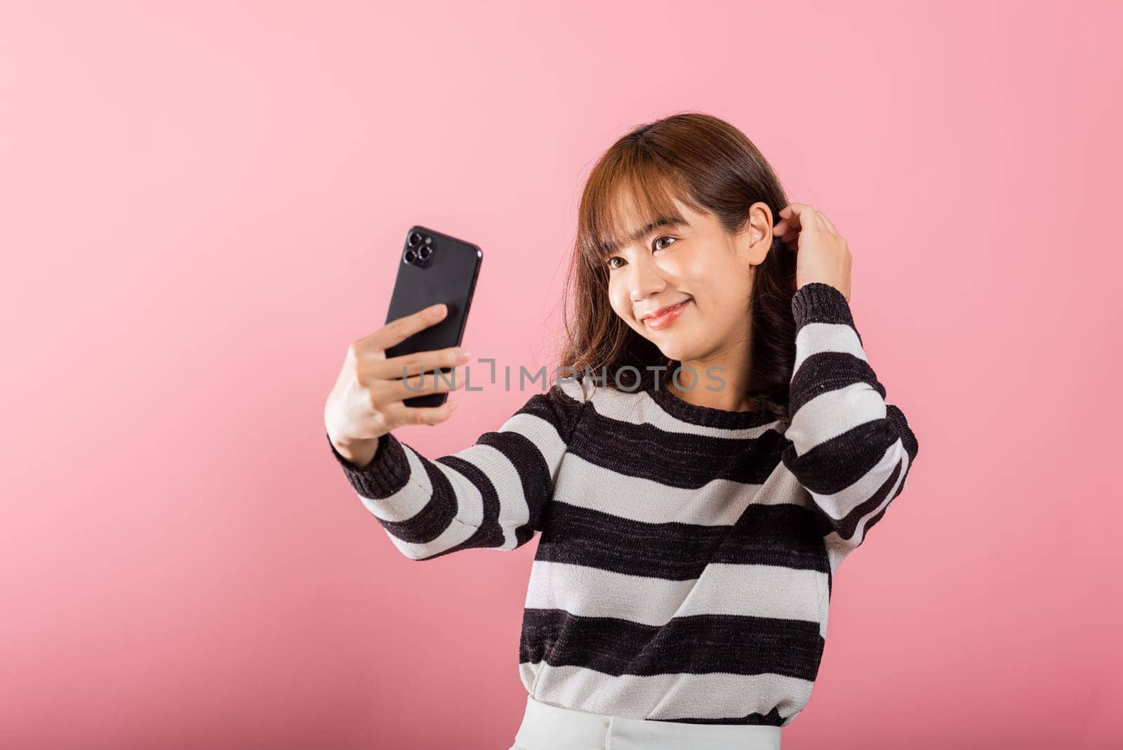 Happy Asian portrait beautiful cute young woman smiling excited making selfie photo, video call on smartphone studio shot isolated on pink background, female hold mobile phone raise hand say hello