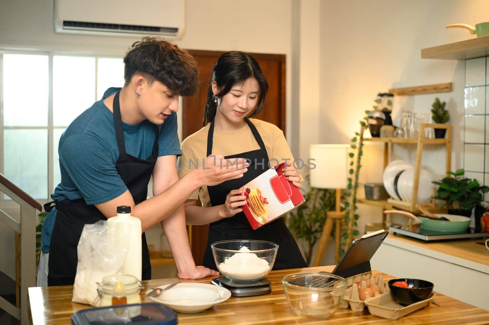 Happy young couple following recipe and measuring pancake mix together in a kitchen.