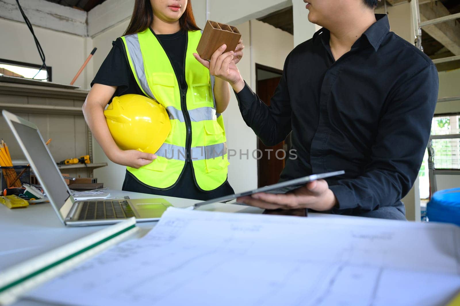 Architects discussing material sample and reviewing design plans at a renovation site.