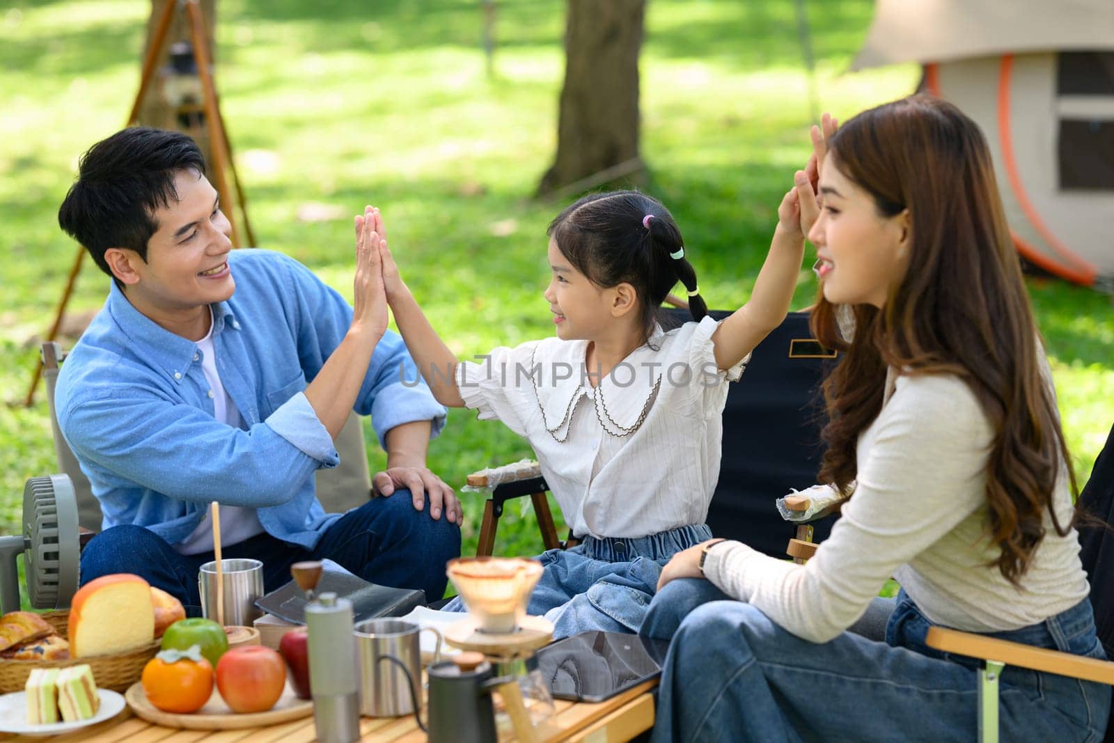 Happy family camping together and enjoying outdoor breakfast in the park.