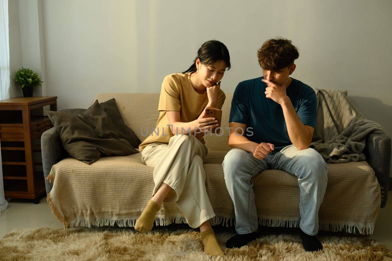 Happy young couple using smartphone together in the living room.