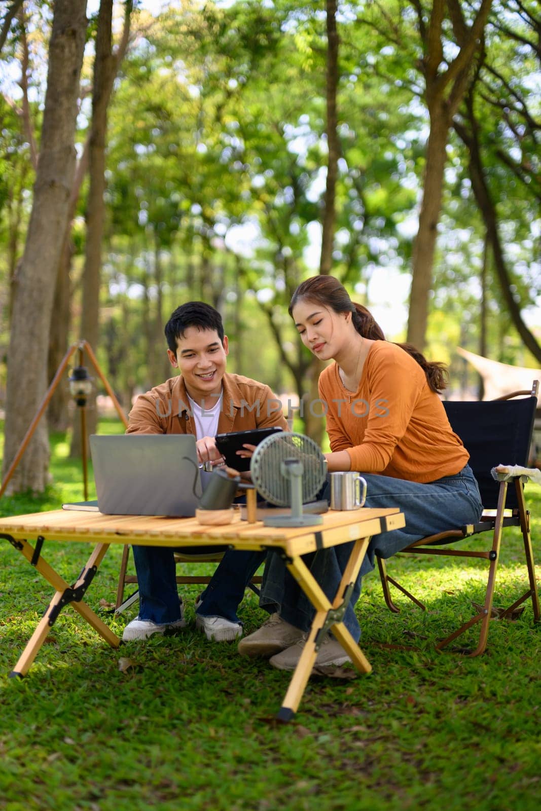 Couple using laptop and digital tablet at a campsite in the forest.