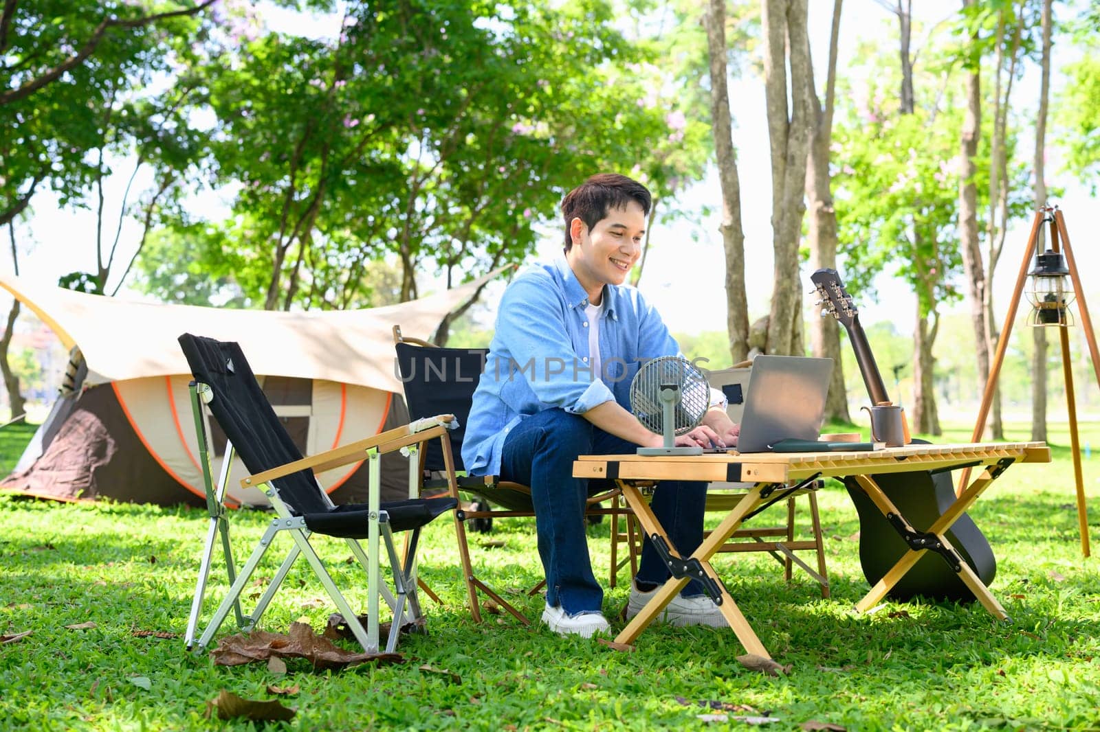 Young man using laptop at a table while camping in the forest.