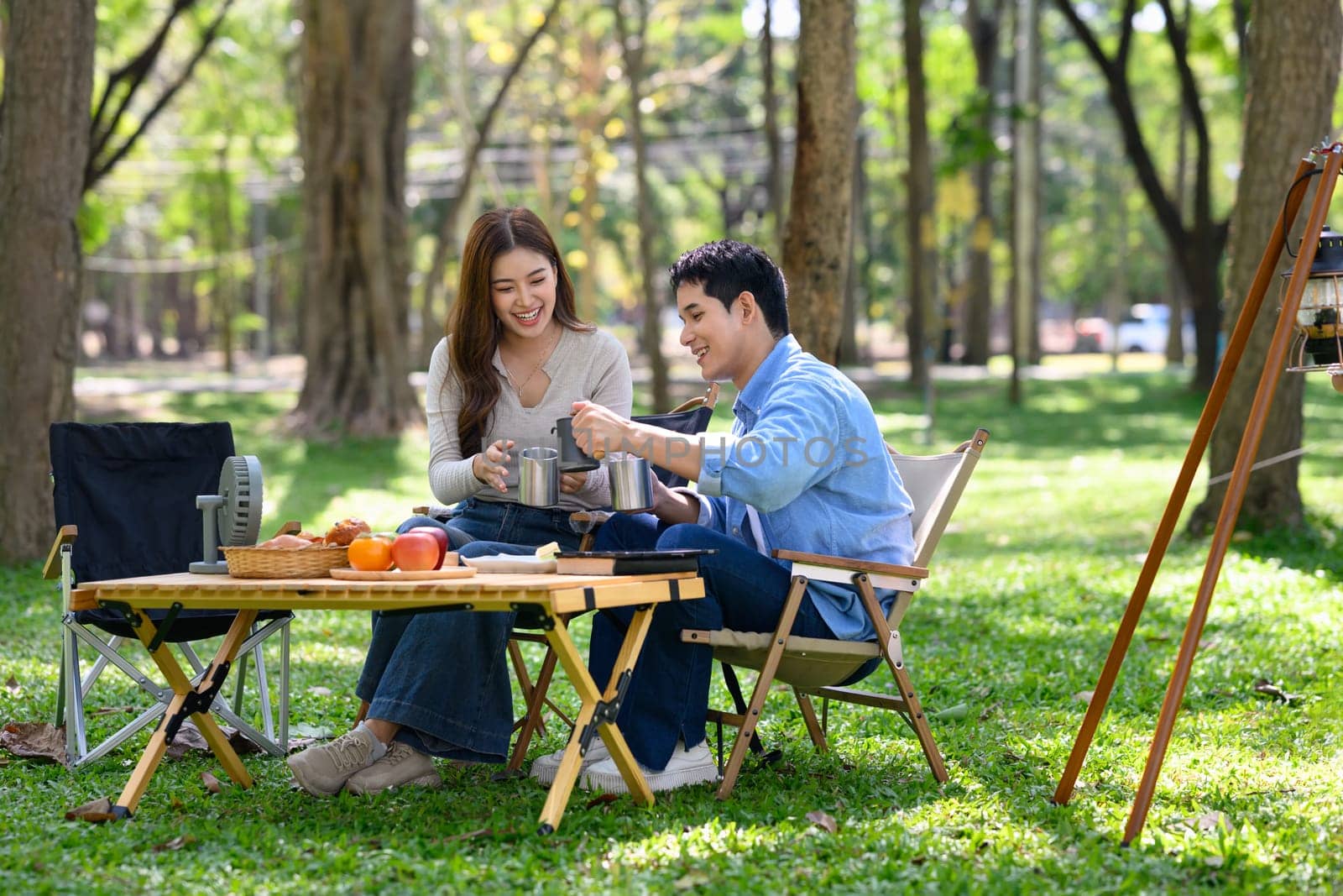 Smiling couple enjoying coffee together at a peaceful campsite surrounded by nature.