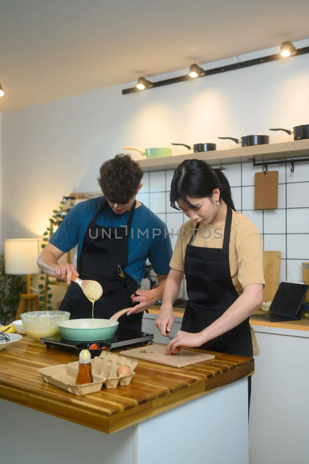 Man and woman wearing aprons and preparing breakfast together in the kitchen.