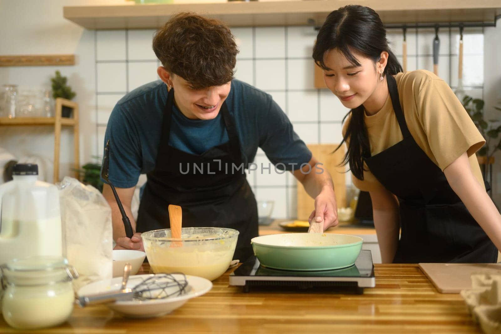 Man and woman wearing aprons and preparing breakfast together in the kitchen.