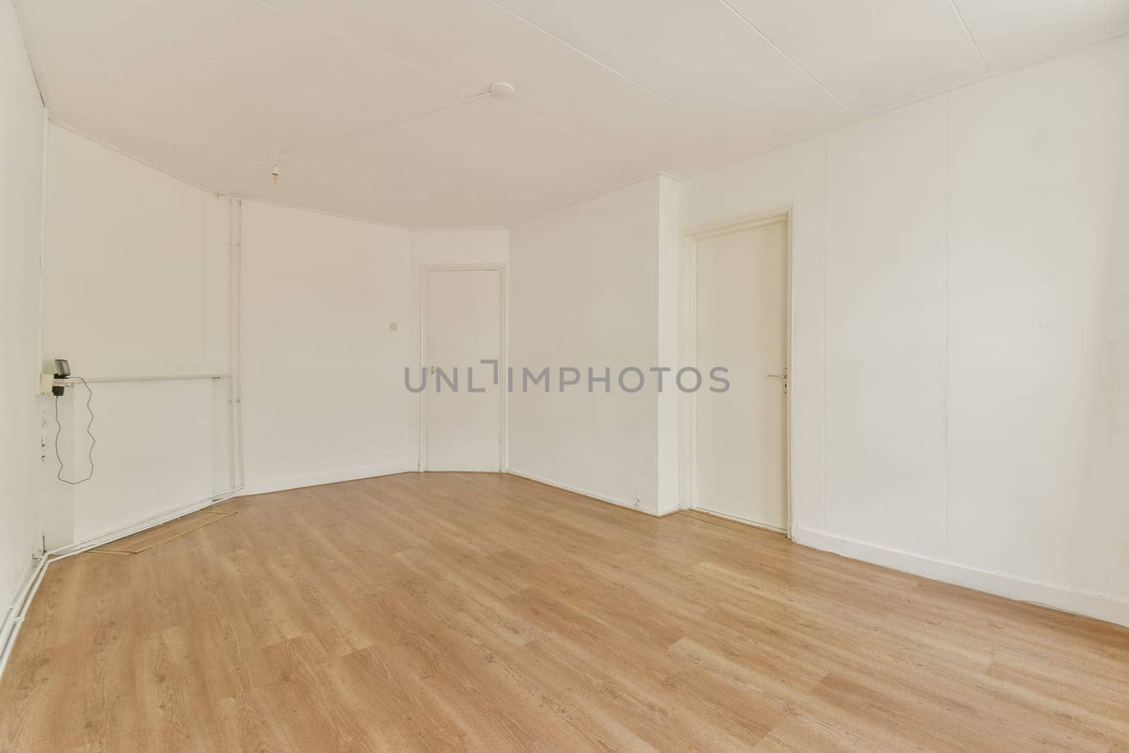 An empty, well-lit interior room showcasing light wooden flooring and plain white walls, offering a clean and minimalist aesthetic.