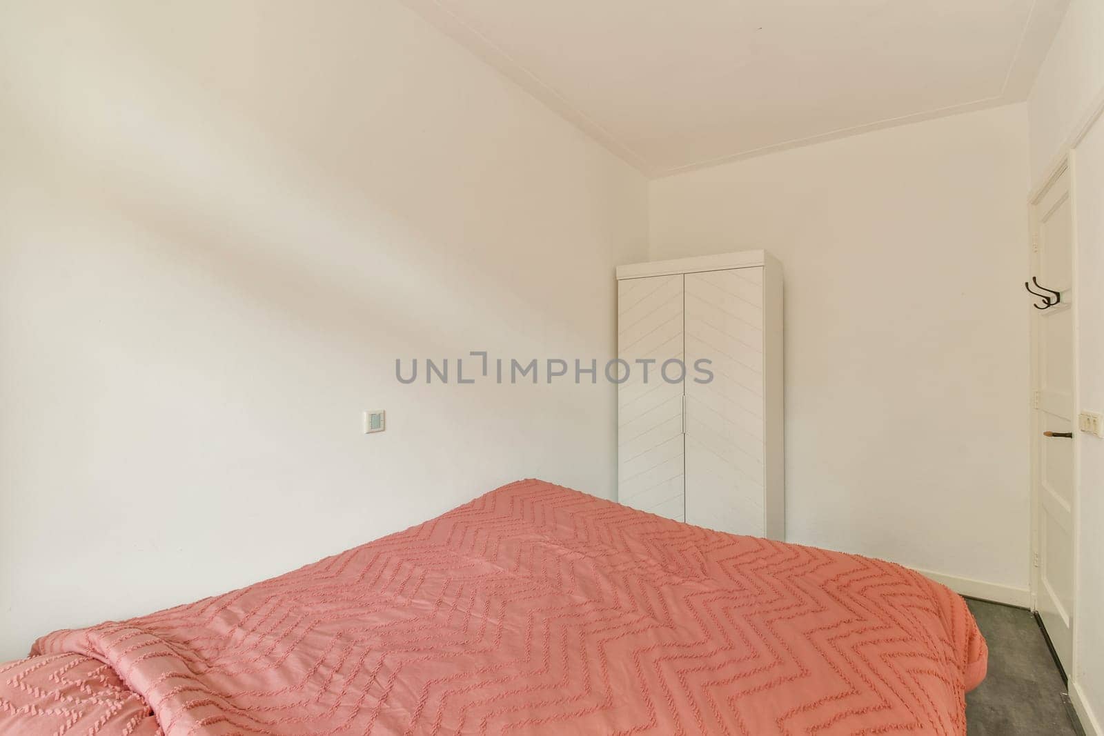 A tranquil minimalist bedroom featuring a neatly made bed with soft, textured textiles, a wardrobe, and subtle wall colors. Ideal for relaxation and simplicity.