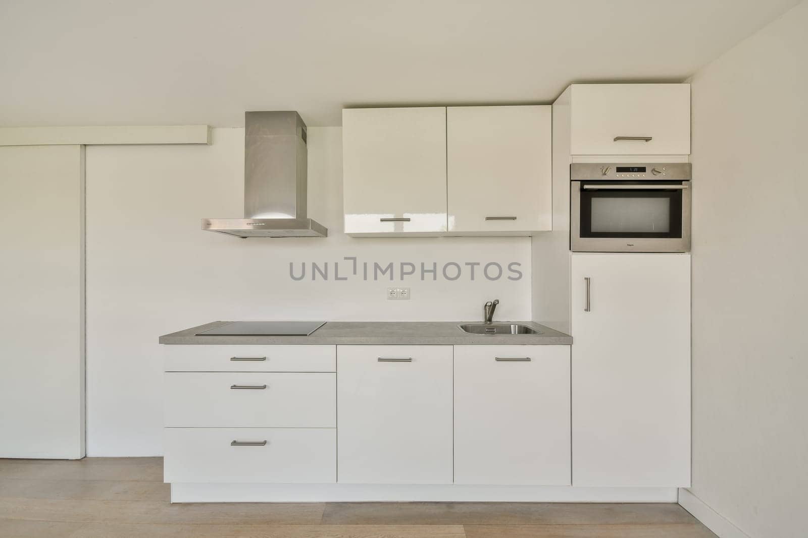 A sleek, modern kitchen featuring white cabinetry, a stainless steel range hood, and integrated appliances. The design emphasizes simplicity and functionality.