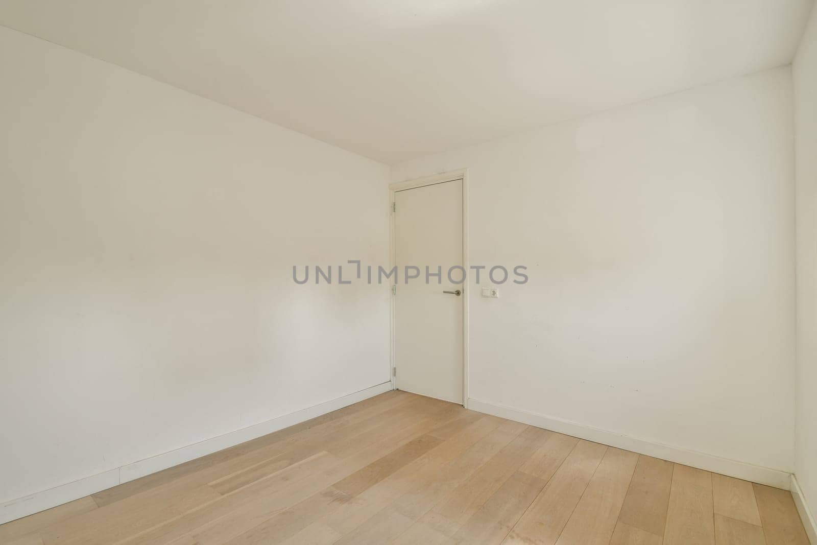 A spacious and minimalist interior featuring plain white walls and wooden flooring, creating a serene atmosphere ideal for various uses.