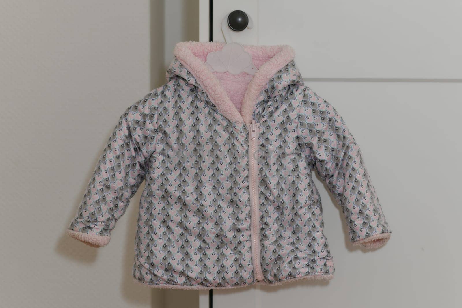 Pink-lilac colored fur jacket for girl hanging on hanger on white background