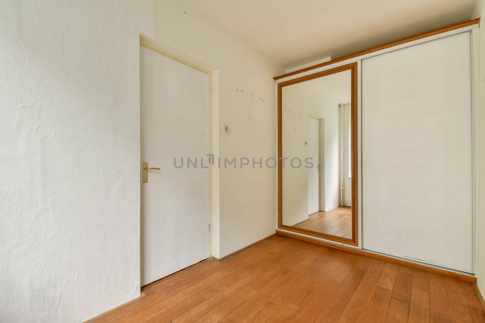 A spacious and bright hallway featuring light-colored walls, hardwood flooring, and a mirrored closet door reflecting the minimalist design.