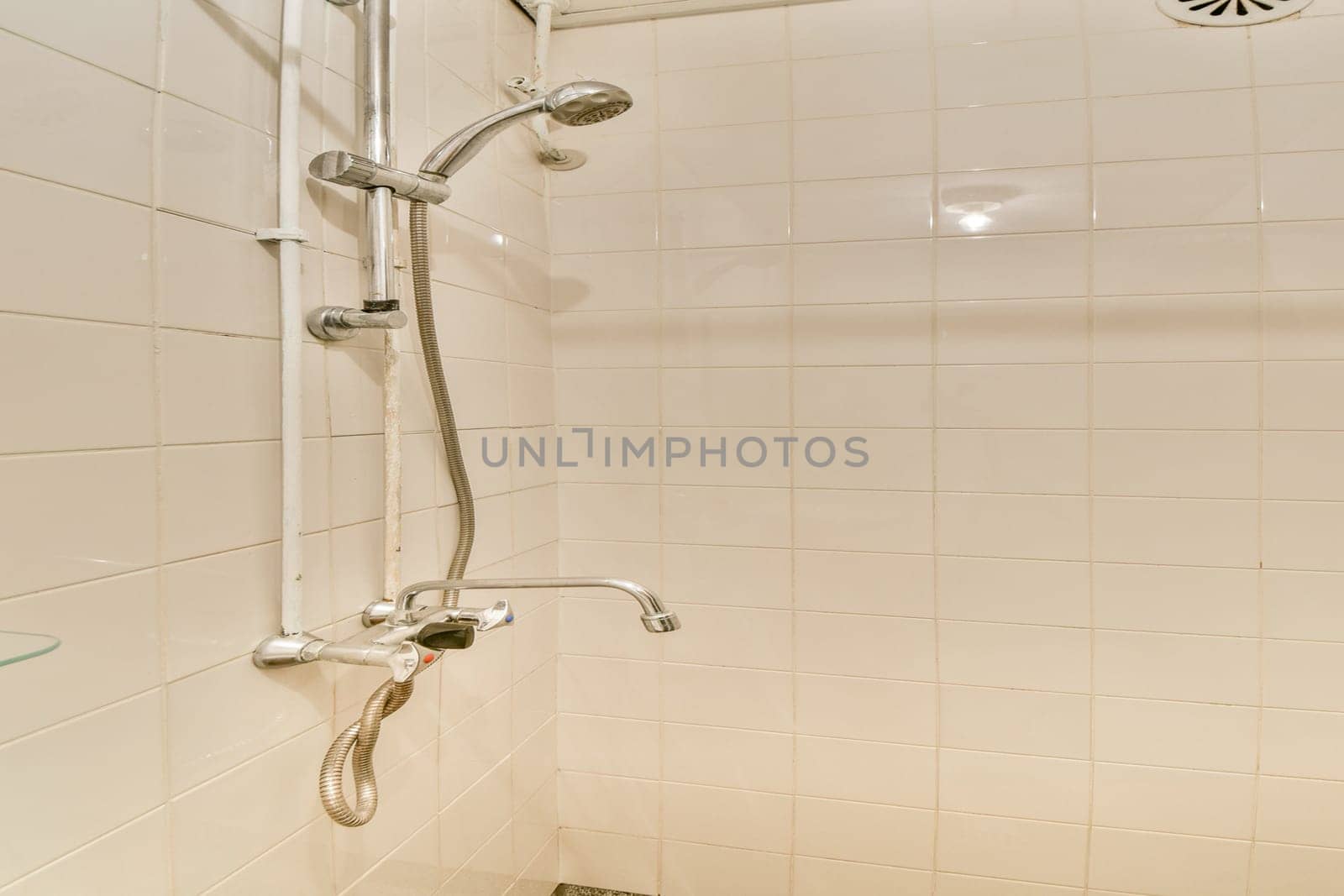 A clean and minimalistic shower area featuring white tiled walls, stainless steel fixtures, and a glass shelf, showcasing contemporary bathroom design.
