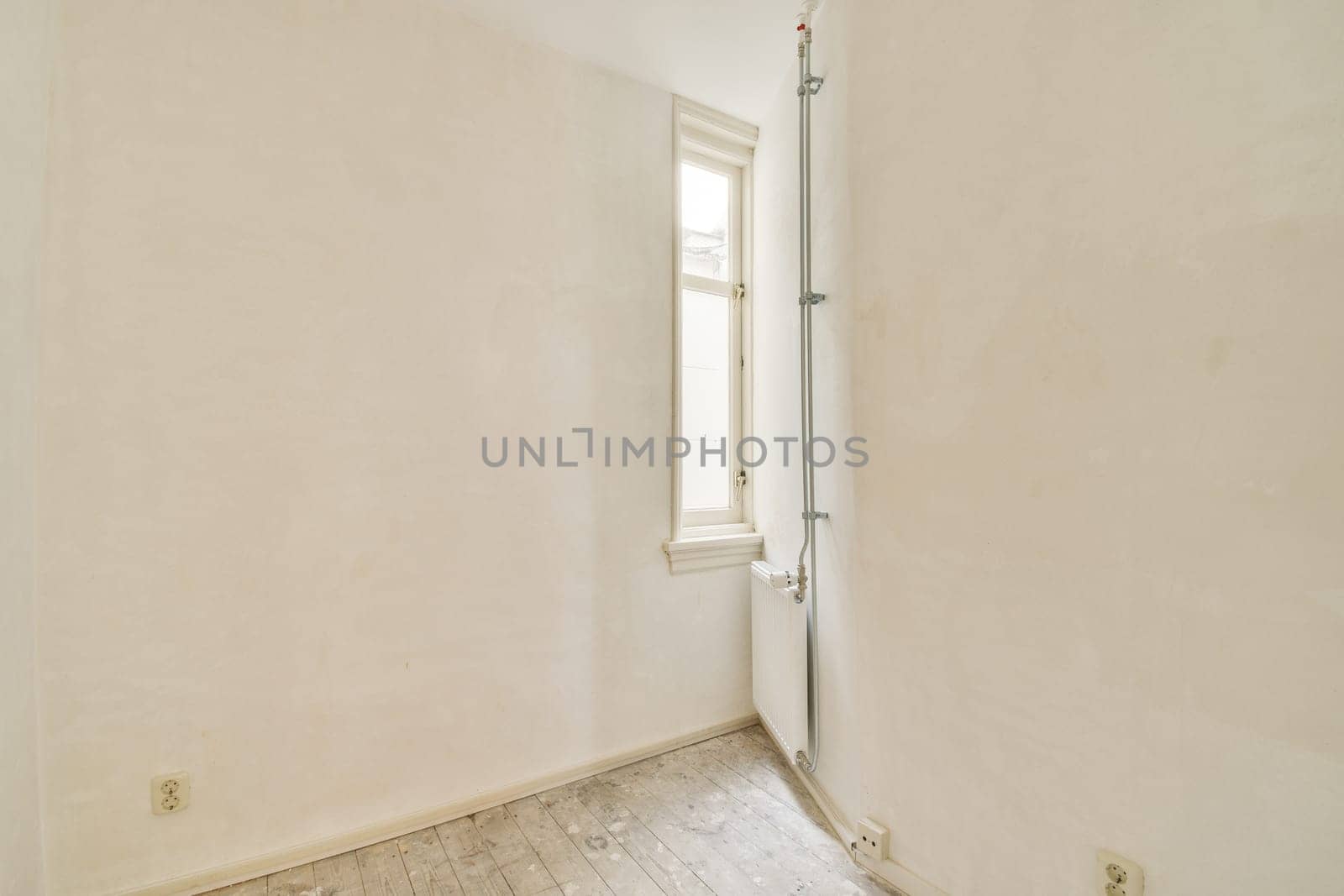 An empty room featuring minimalist white walls and a single window allowing natural light to illuminate the space. The flooring is simple and unobtrusive.