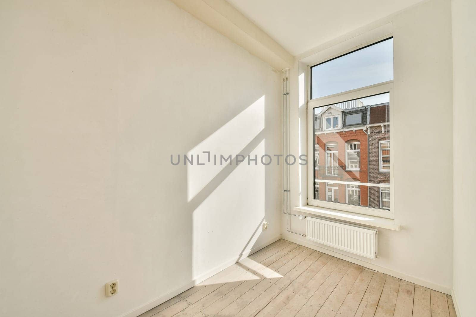 A spacious room featuring a large window that allows natural light to illuminate the area, showcasing its minimalistic design and light-colored flooring.
