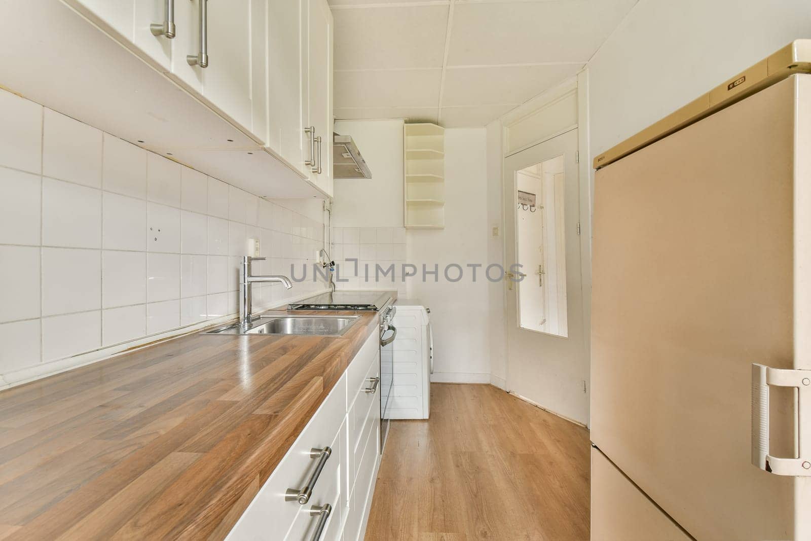 A contemporary kitchen space featuring sleek white cabinetry, a wooden countertop, and minimalistic design elements. The room is well-lit and functional.