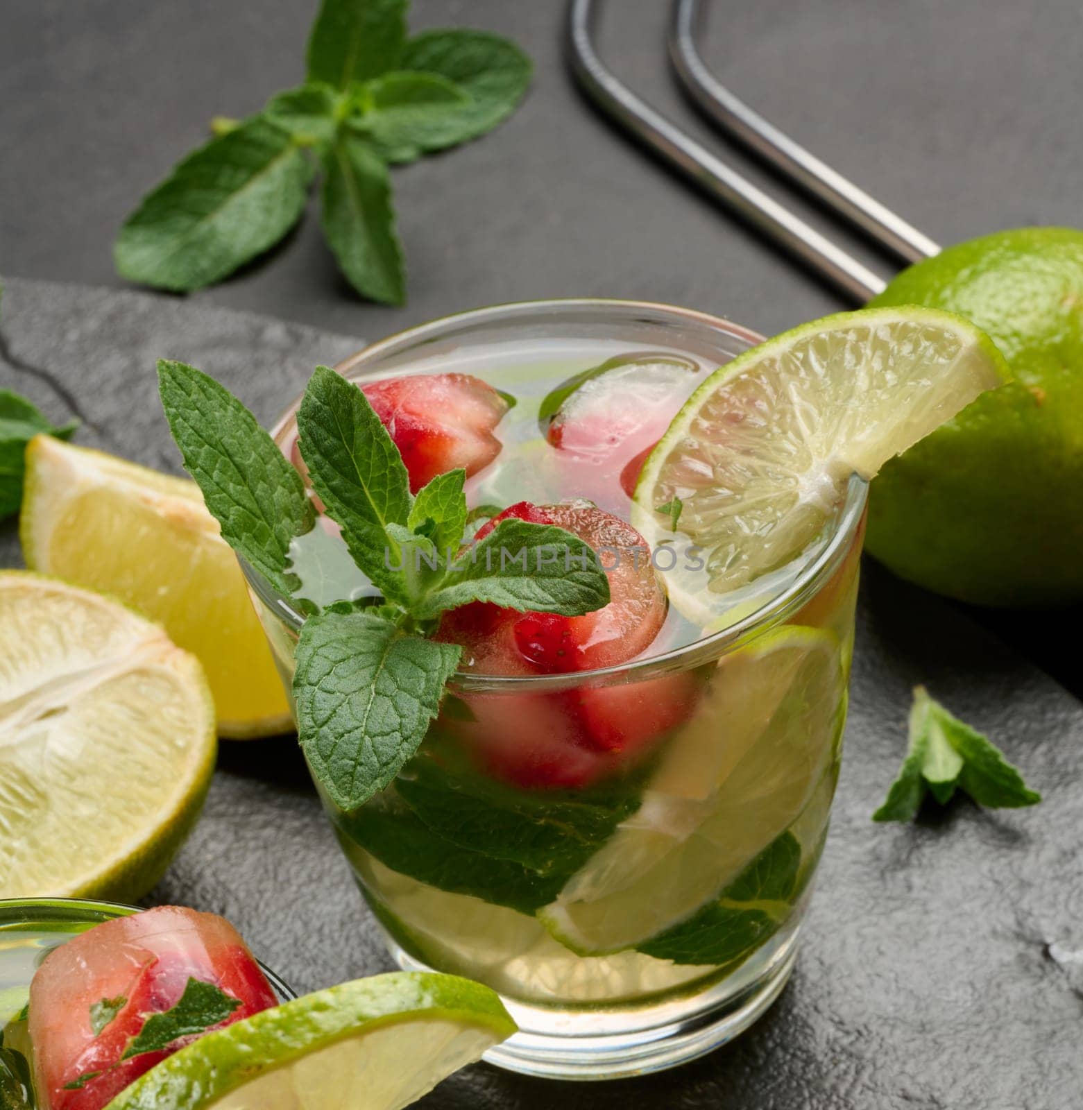 Refreshing mojito cocktail with lime, mint, strawberry, and ice on dark background