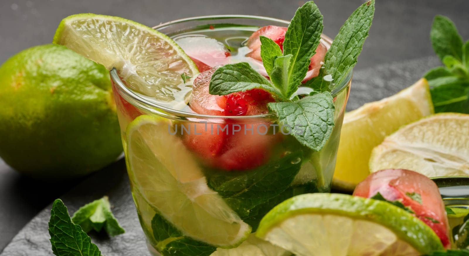 Refreshing mojito cocktail with lime, mint, strawberry, and ice on dark background, close up