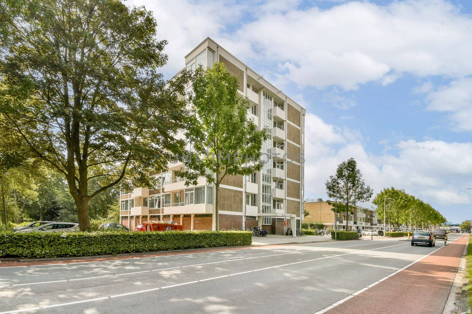 A contemporary multi-story residential building is set against a backdrop of leafy trees and a clear sky, creating a serene neighborhood atmosphere.