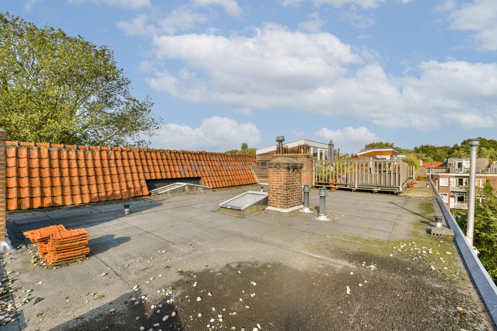 A rooftop scene featuring a mixture of roofing materials and lush greenery under a partly cloudy sky, showcasing urban architecture and nature's presence.