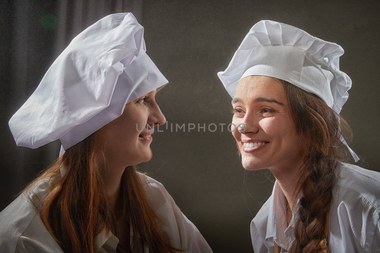 Two female friends are playfully posing with flour during a cheerful cooking session in the kitchen.