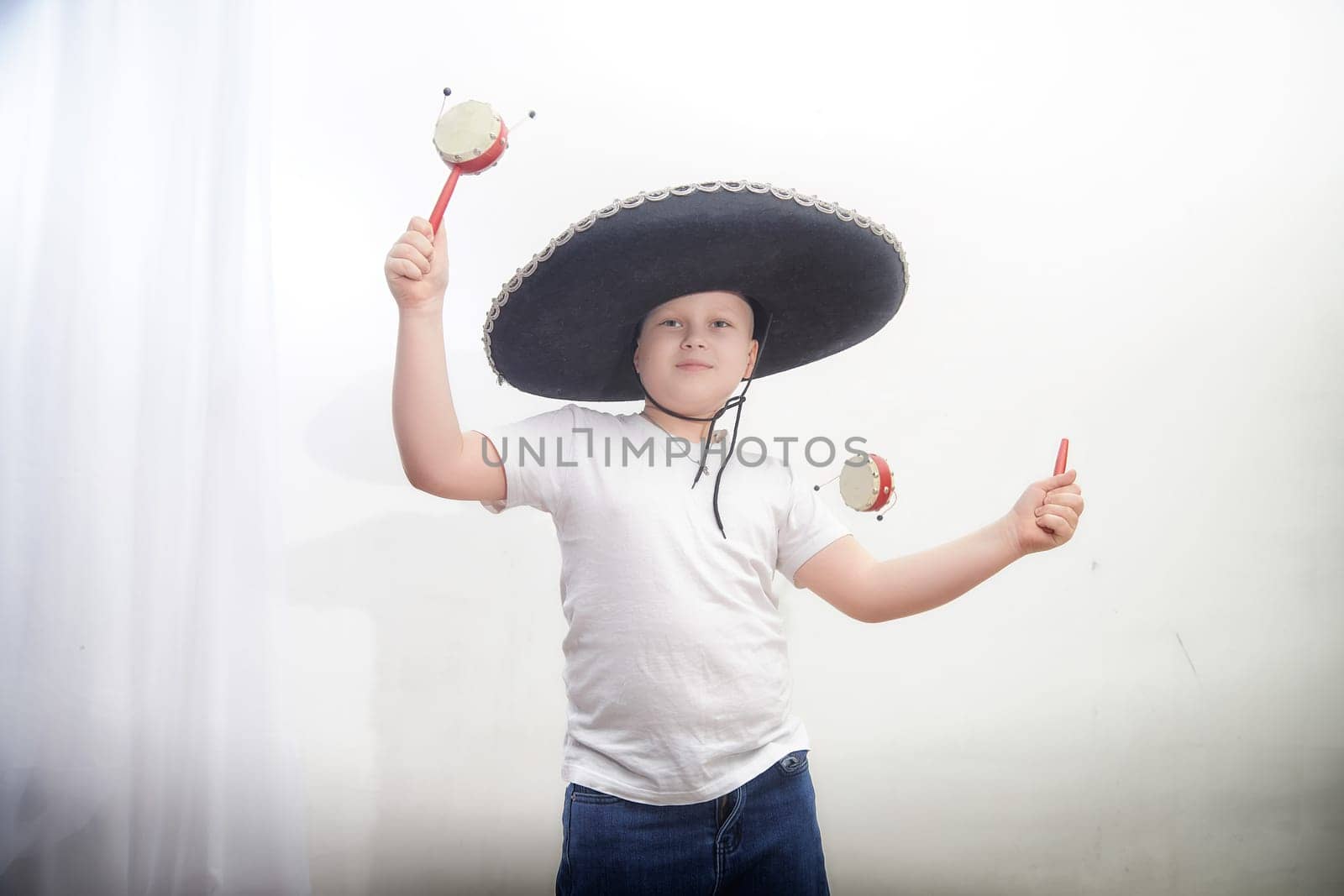 A young boy joyfully engages in a cultural celebration, wearing a traditional sombrero and holding maracas to make music.