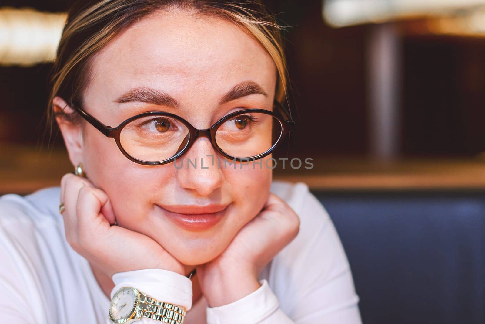 Portrait of a satisfied beautiful young woman wearing glasses in a restaurant looking aside with a smile while waiting for an order. High quality photo
