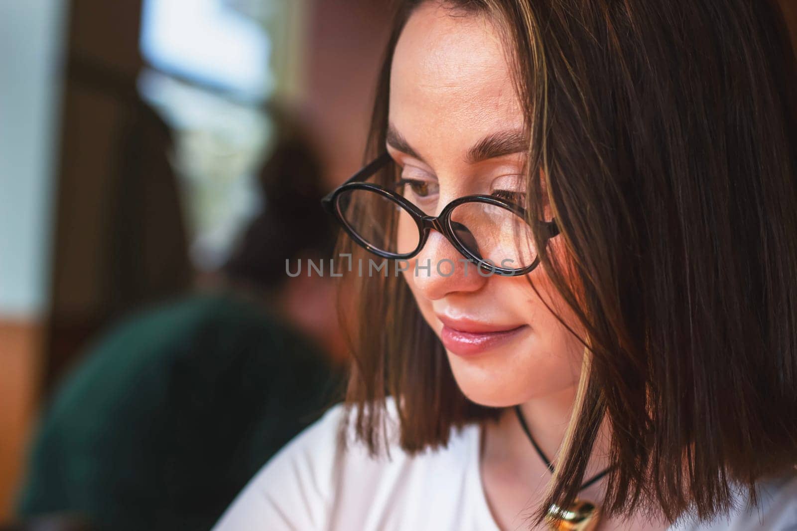 Portrait of a satisfied beautiful young woman wearing glasses in a restaurant looking aside with a smile while waiting for an order. High quality photo