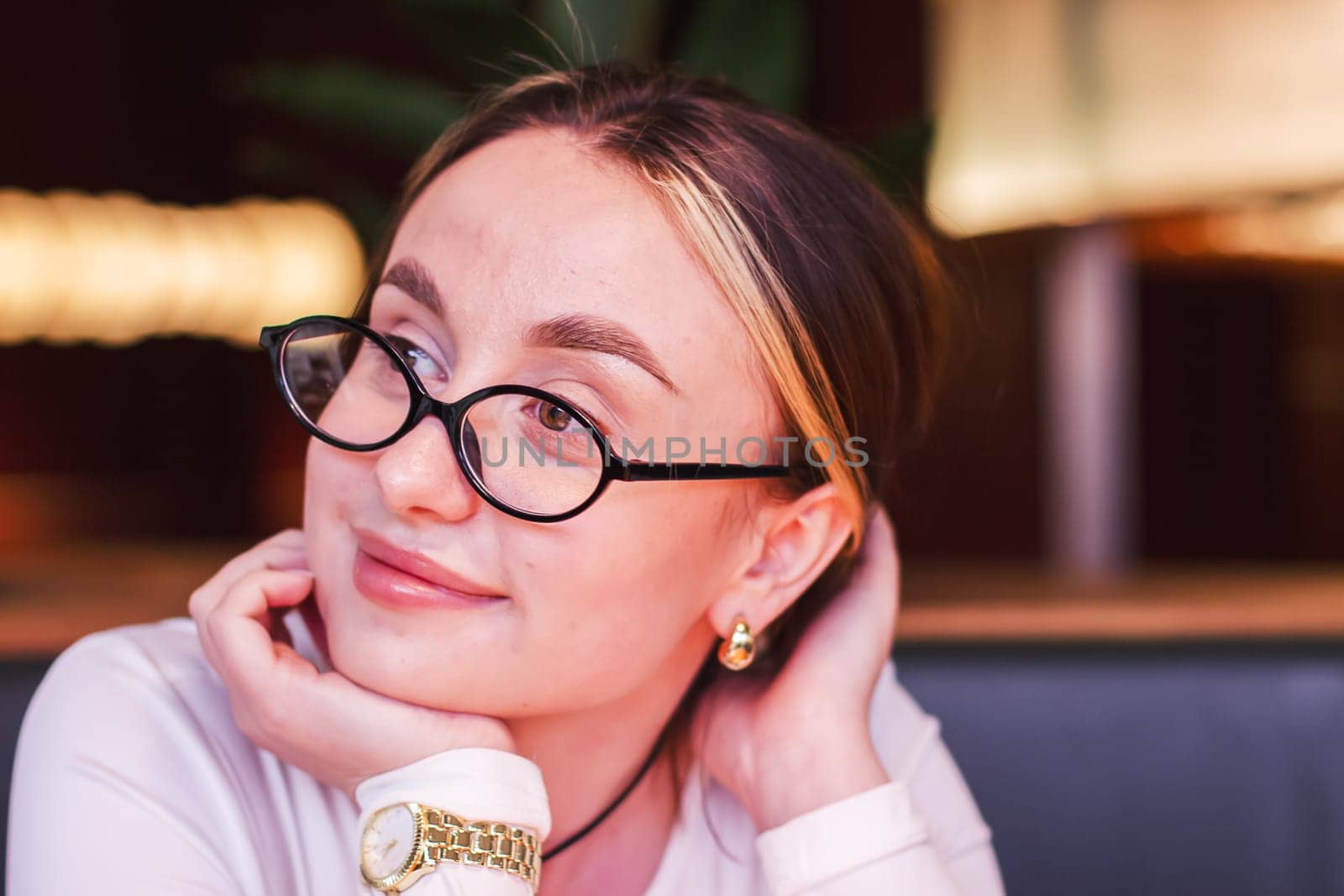 Portrait of a satisfied beautiful young woman wearing glasses in a restaurant looking aside with a smile while waiting for an order. High quality photo