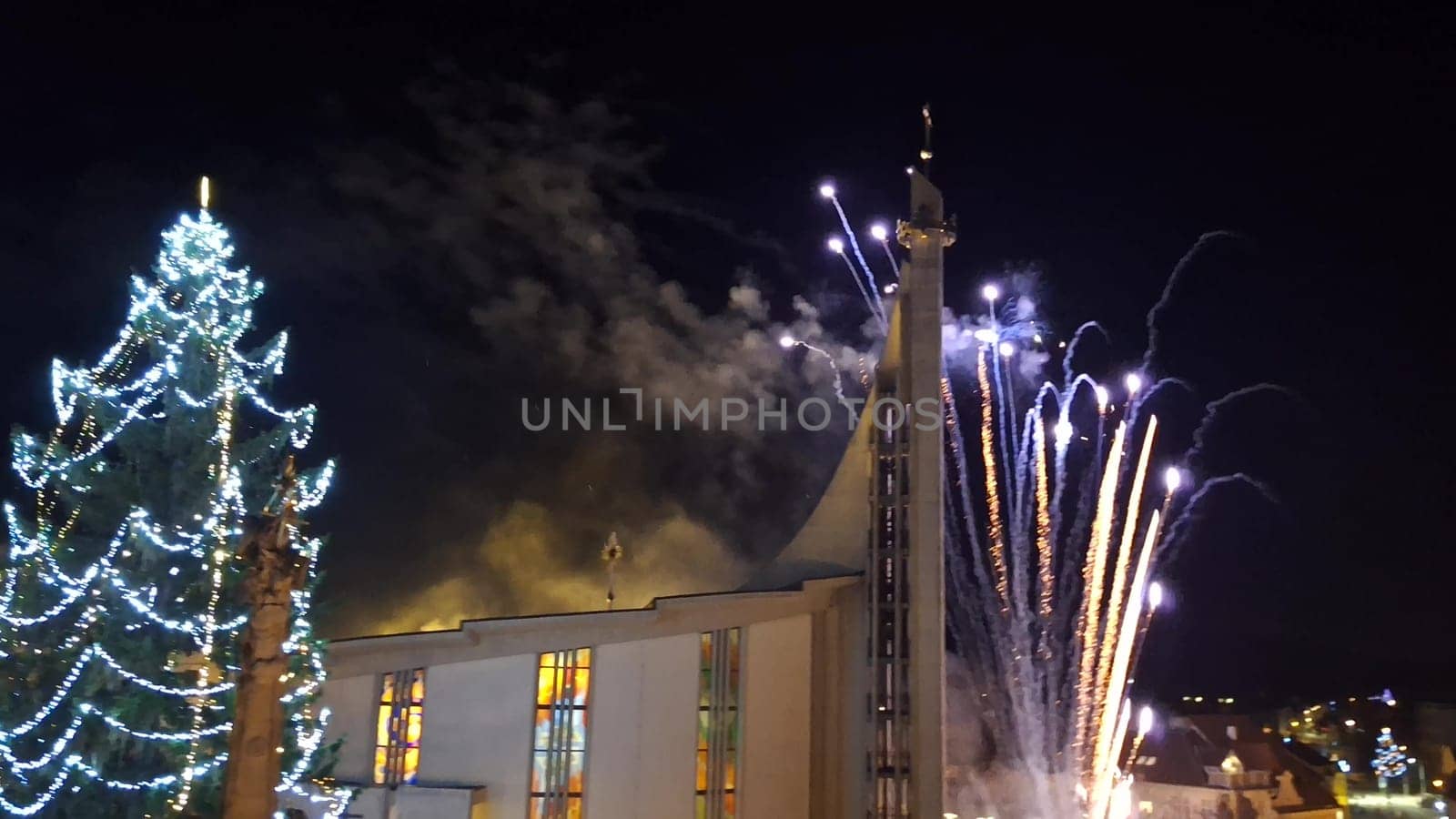 Fireworks during Christmas. View of the illuminated Christmas tree and fireworks over the church in the town.