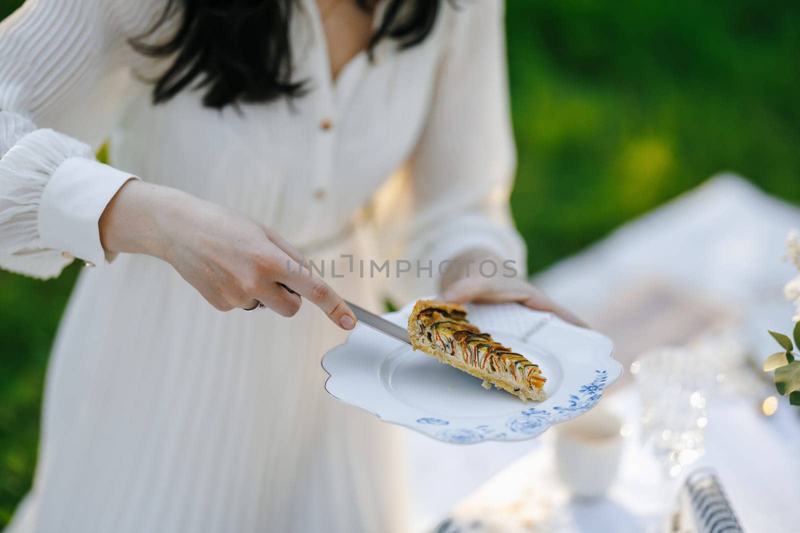 A woman is carefully cutting a delicious piece of pie that is placed on a decorative plate for her to enjoy later