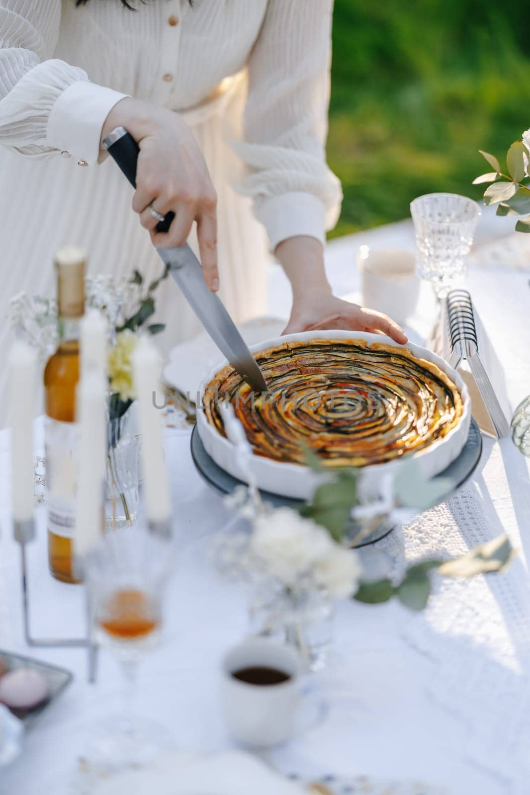 A woman is carefully cutting a delicious pie that is placed on a table, skillfully preparing it for serving to her guests