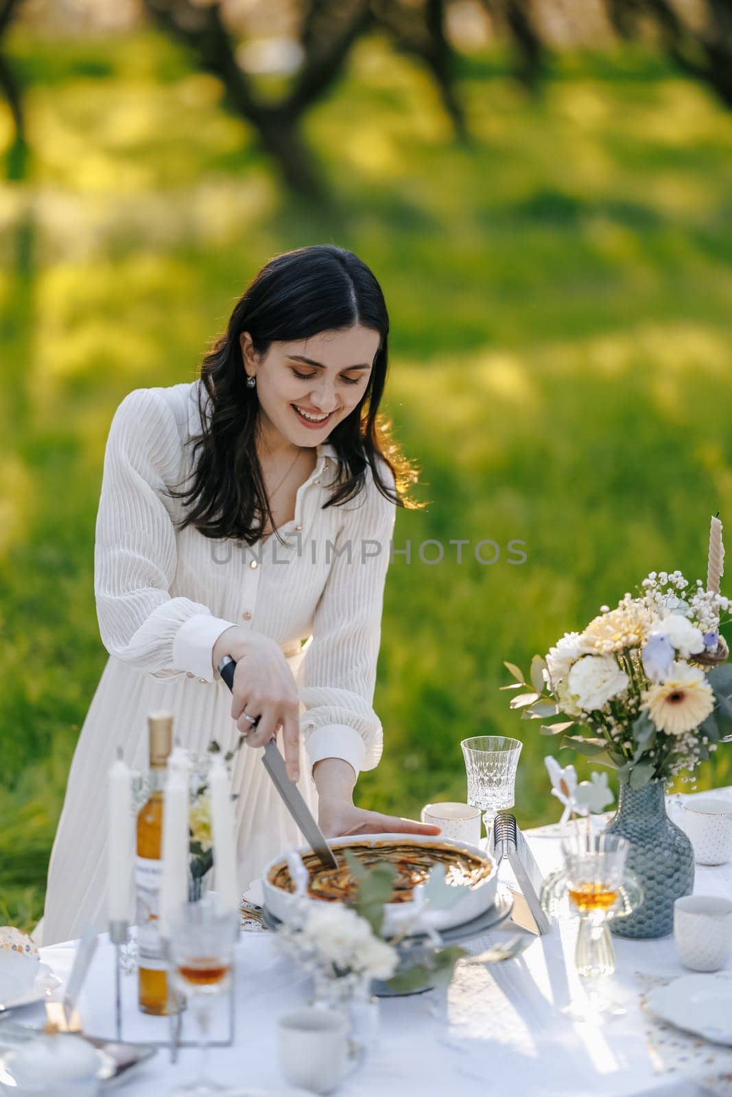 A woman is skillfully cutting a delicious piece of cake on the beautifully set table that is arranged for a delightful occasion