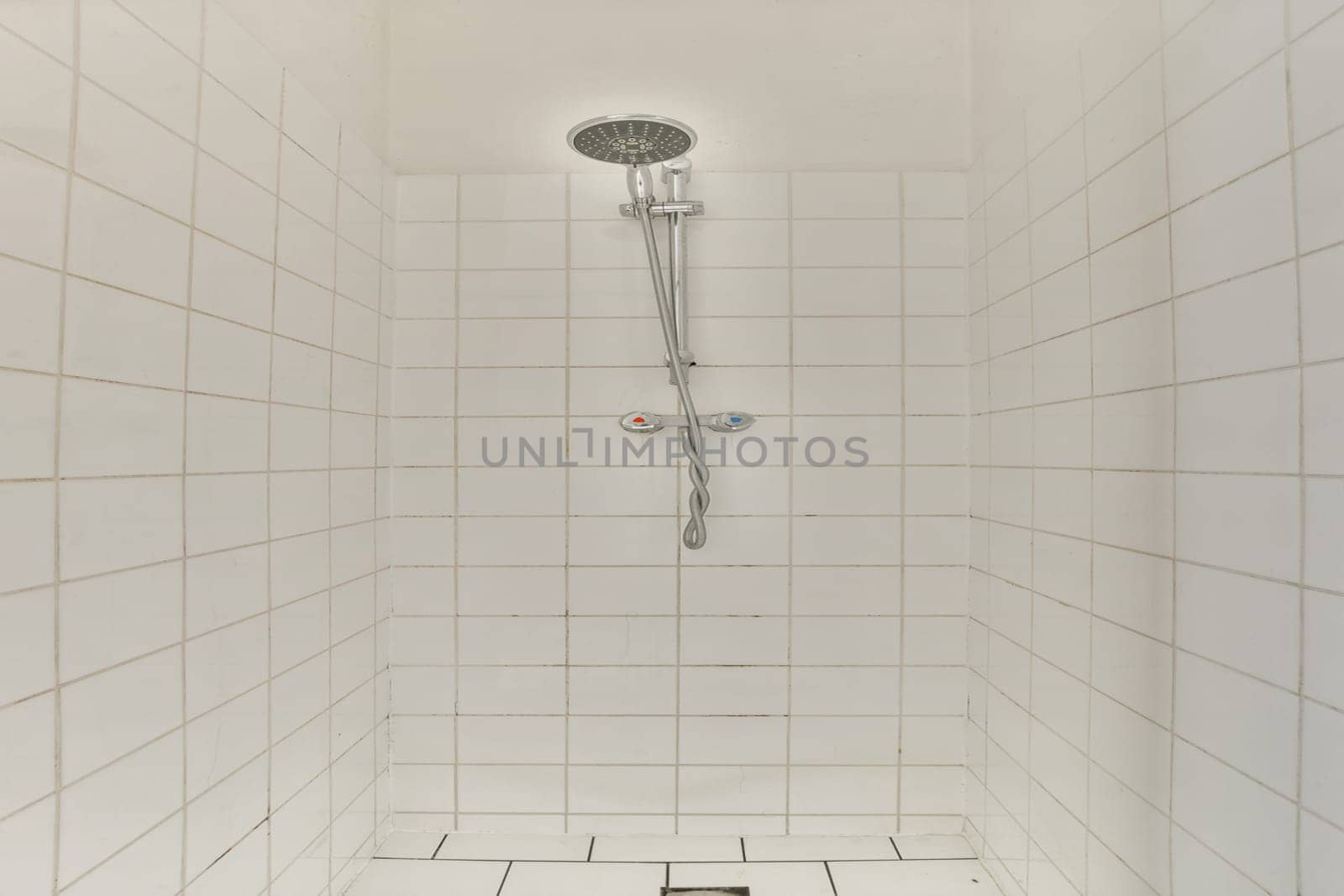 A sleek shower stall featuring white tiled walls and a contemporary showerhead. The minimalist design offers a clean and refreshing aesthetic.