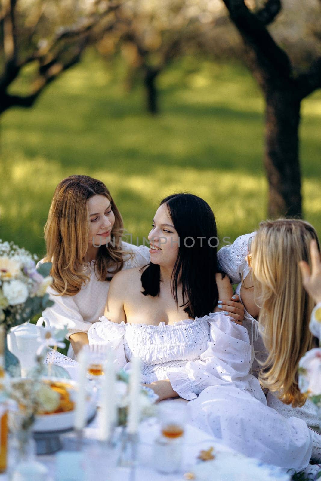 Three women are comfortably seated around a table in a lovely park, enjoying each others company amidst the beauty of nature