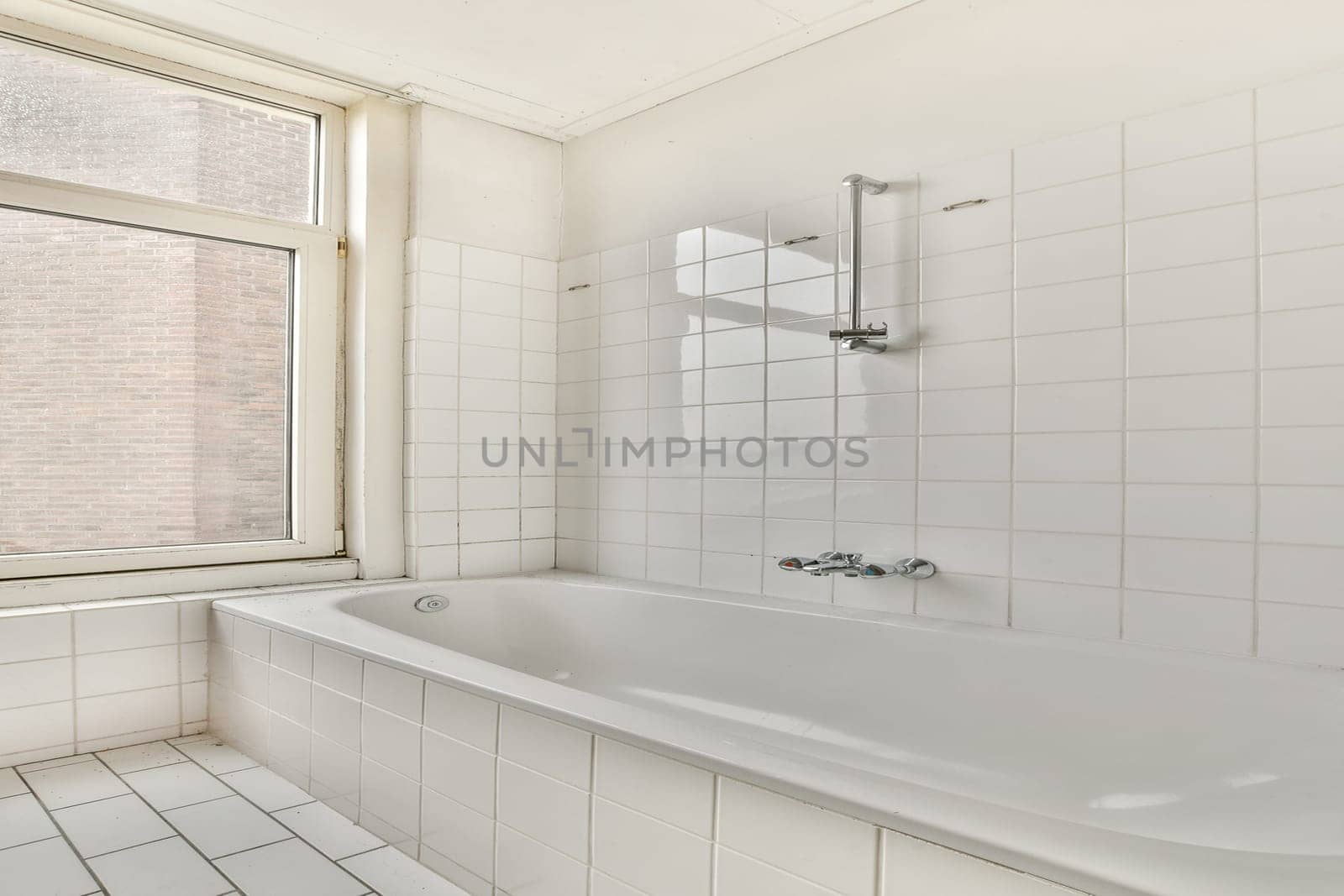 A bright and minimalist bathroom showcasing a bathtub, large window, and white tiled walls. The interior emphasizes simplicity and cleanliness.