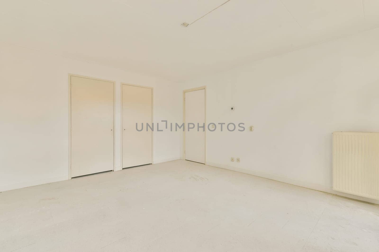 A vacant room showcasing white walls, bare floor, and a simplistic design. The space is illuminated with natural light, emphasizing the minimal decor.
