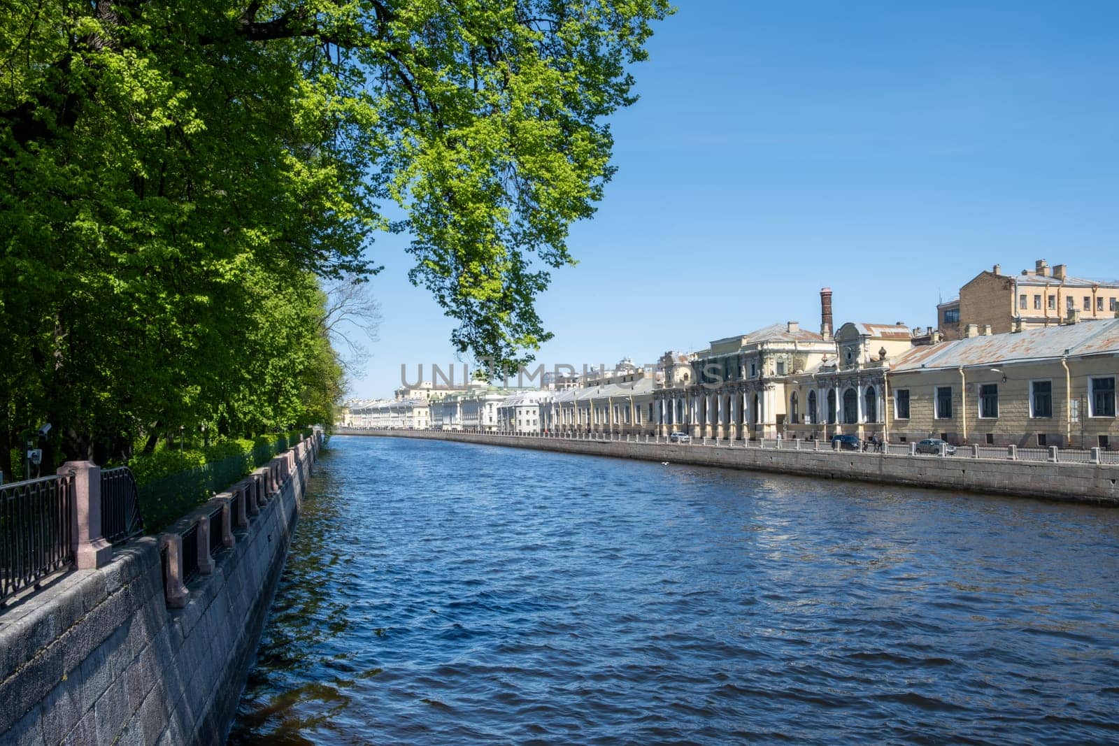 Saint-Petersburg, Russia - 05.21.24. Urban riverside scene captures a serene Fontanka river lined with historic architecture and lush greenery under a clear sky