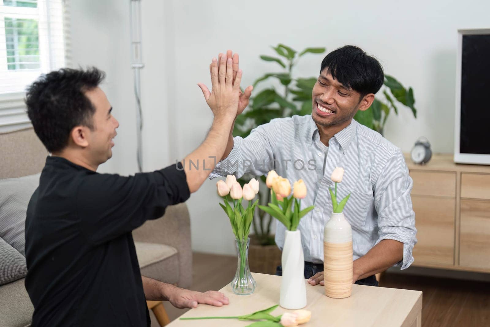 Two friends engage in a playful high-five, surrounded by flowers, symbolizing their friendship and connection in a warm and inviting space.