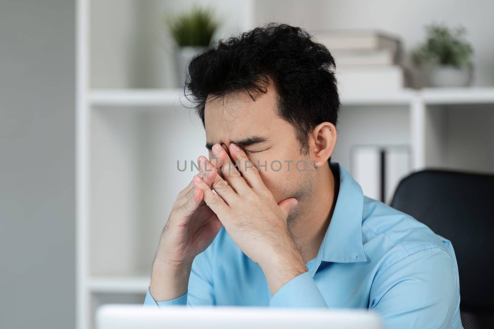 An office worker experiencing a headache from overwork, sitting at a desk in a modern office setting.