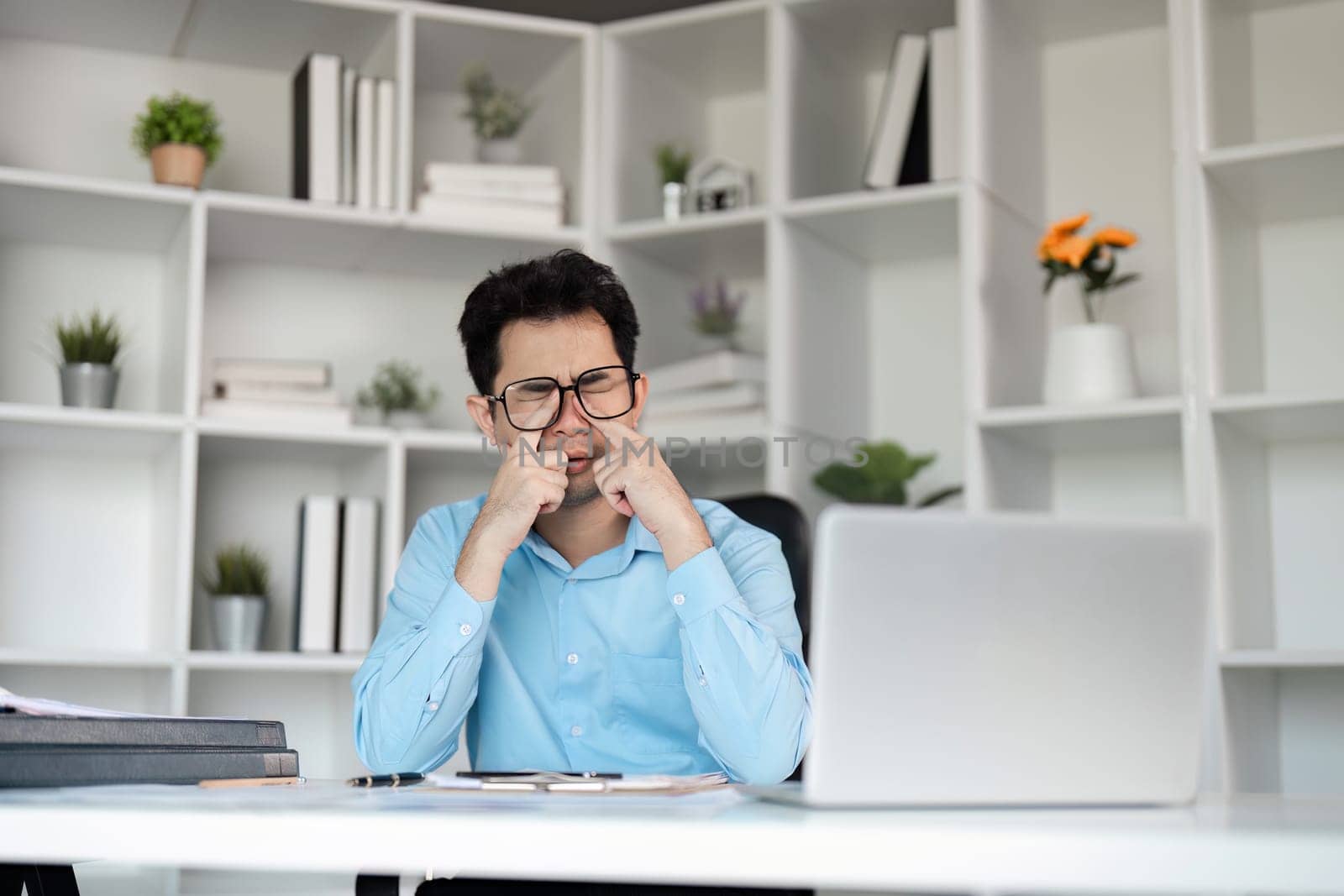 Office worker feeling overwhelmed and tired, suffering from a headache due to a demanding work schedule in a contemporary office setting.