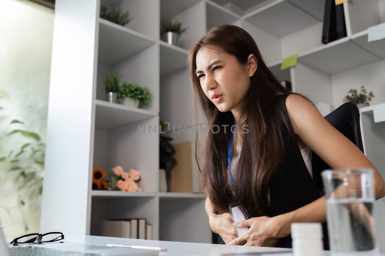 A businesswoman experiencing discomfort while working in a contemporary office setting, highlighting workplace health challenges.