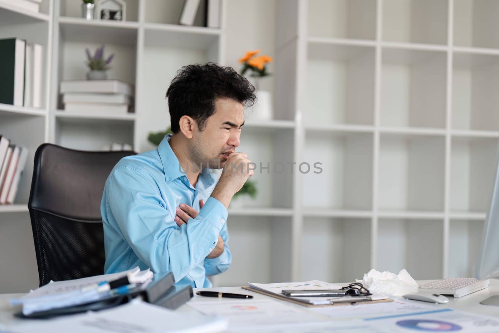An office worker sits at their desk, visibly unwell with a cold, surrounded by work materials in a modern office setting.