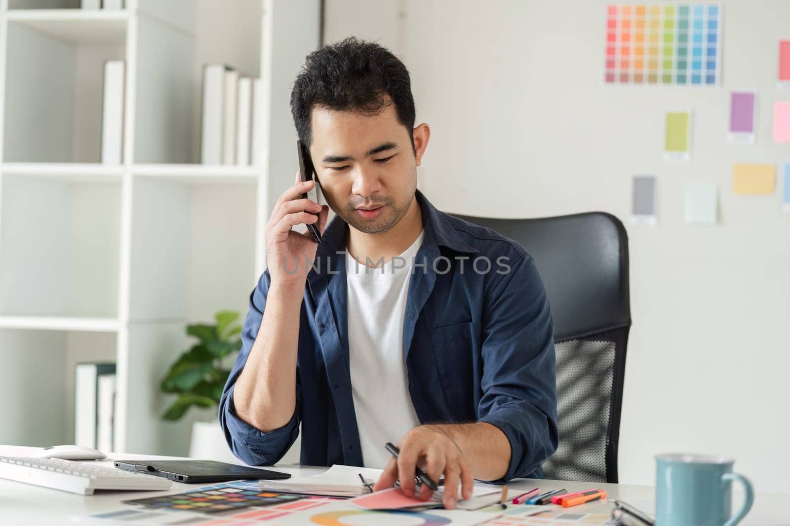 Graphic designer in a studio setting, surrounded by design tools and color samples, focused on creative work.