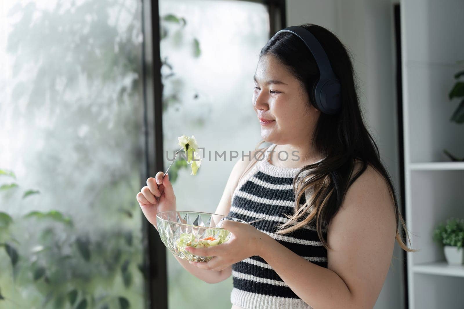 A young woman with headphones enjoys a fresh salad, promoting healthy eating habits and a balanced lifestyle.